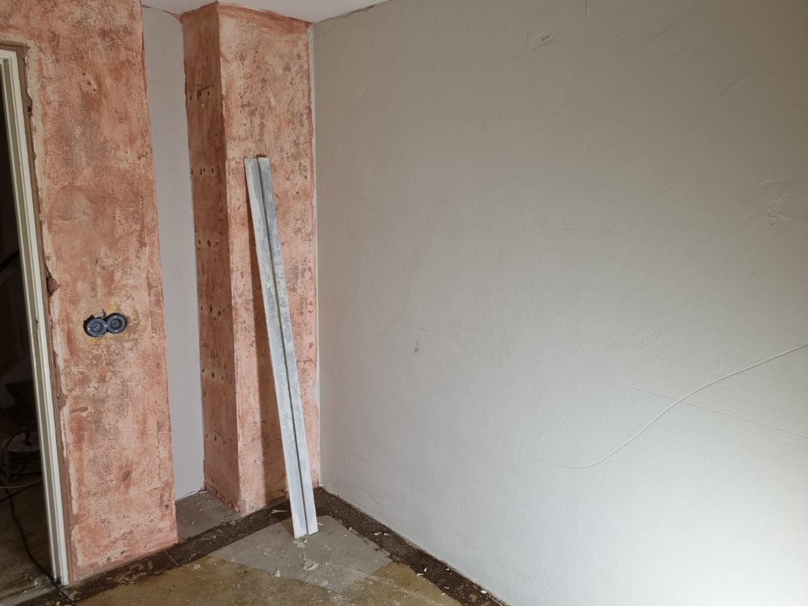 Een wand in wording: links de roze onderlaag, rechts een gladde gestucte muur